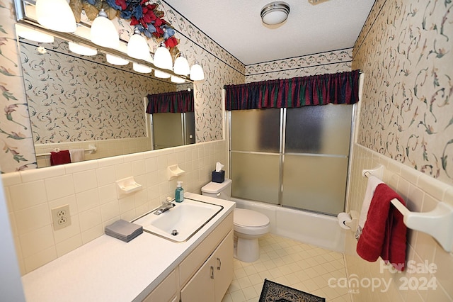 full bathroom with tile walls, bath / shower combo with glass door, a textured ceiling, and toilet