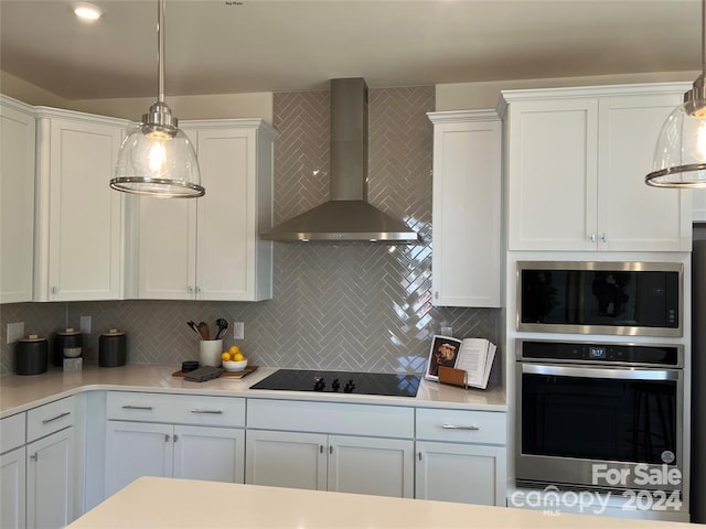 kitchen featuring wall chimney range hood, stainless steel oven, black electric cooktop, pendant lighting, and white cabinets