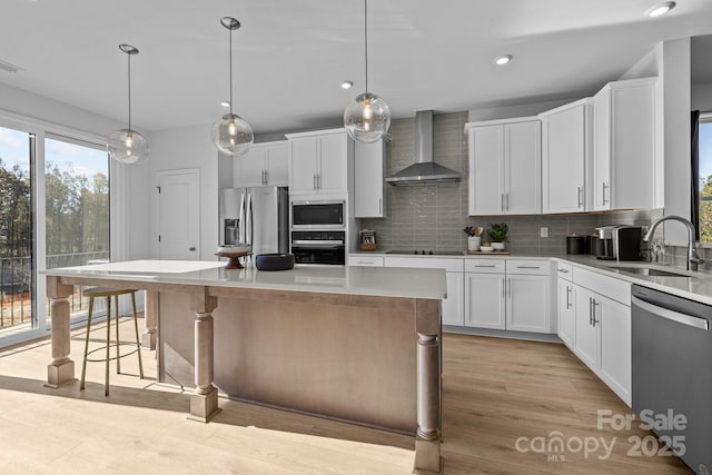 kitchen featuring sink, white cabinetry, a kitchen island, wall chimney range hood, and black appliances