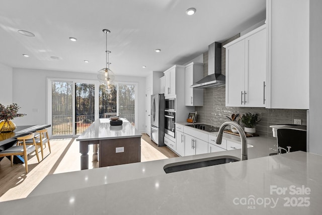 kitchen with wall chimney range hood, decorative light fixtures, a center island, sink, and white cabinetry