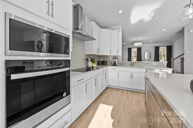 kitchen with built in microwave, hanging light fixtures, wall chimney exhaust hood, black electric stovetop, and white cabinets