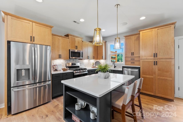 kitchen with a kitchen bar, a center island, stainless steel appliances, decorative light fixtures, and light hardwood / wood-style flooring