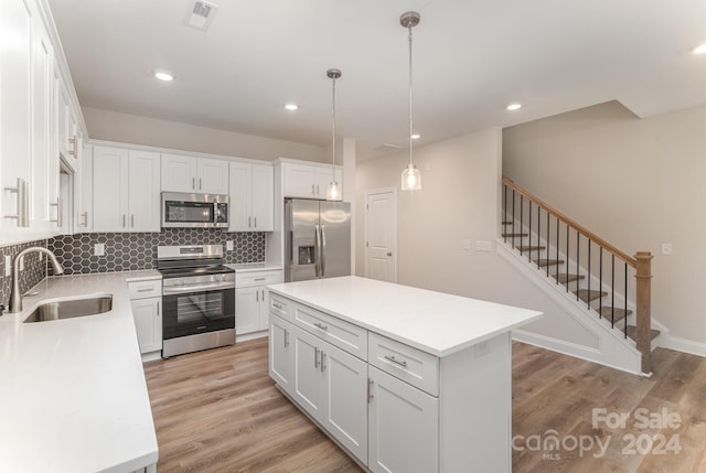 kitchen with light wood-type flooring, stainless steel appliances, sink, white cabinets, and a kitchen island