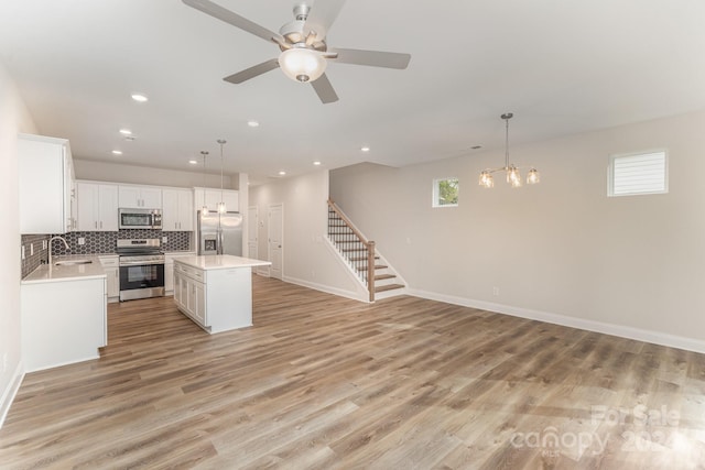 kitchen with white cabinets, hanging light fixtures, light wood-type flooring, a kitchen island, and stainless steel appliances