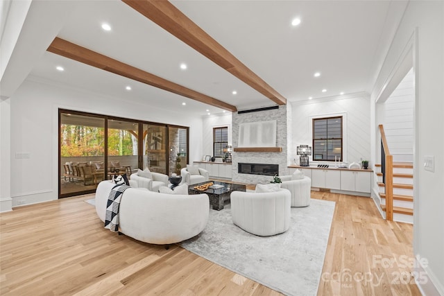 living room with beamed ceiling, a large fireplace, and light hardwood / wood-style flooring