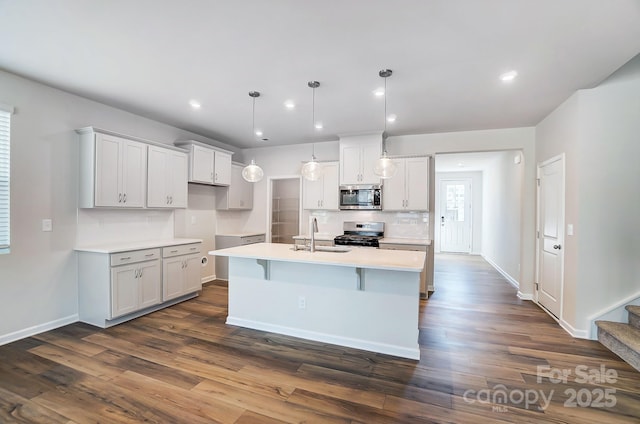 kitchen with appliances with stainless steel finishes, dark wood-type flooring, a sink, and tasteful backsplash