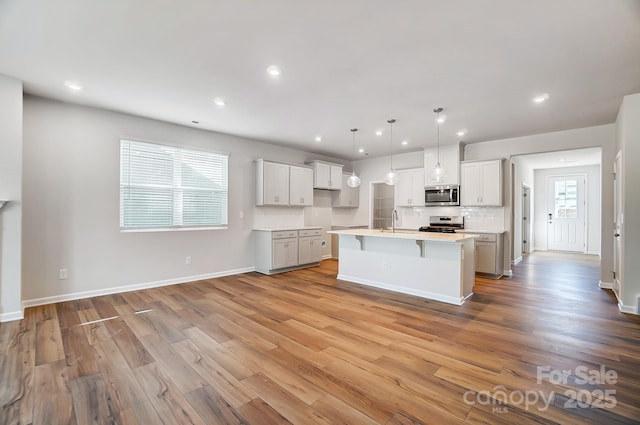 kitchen featuring a breakfast bar, a sink, light countertops, appliances with stainless steel finishes, and light wood-type flooring