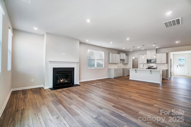 unfurnished living room featuring a wealth of natural light, wood finished floors, visible vents, and recessed lighting