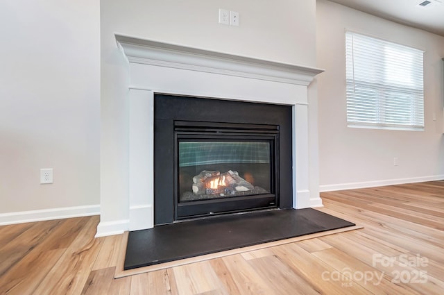 interior details with wood finished floors, a glass covered fireplace, visible vents, and baseboards