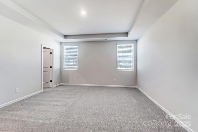 spare room featuring a tray ceiling, carpet flooring, and baseboards