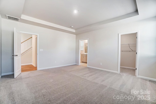 unfurnished bedroom with visible vents, baseboards, light colored carpet, a tray ceiling, and a walk in closet