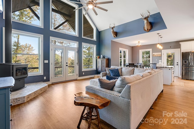 living room with light hardwood / wood-style floors, high vaulted ceiling, a wood stove, and ceiling fan with notable chandelier