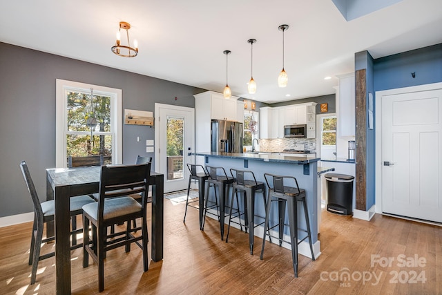 kitchen with white cabinets, stainless steel appliances, decorative light fixtures, and light wood-type flooring