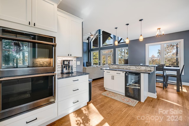 kitchen featuring double oven, white cabinets, hanging light fixtures, and light hardwood / wood-style floors