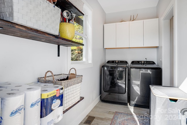 clothes washing area featuring washing machine and dryer, light wood-type flooring, and cabinets