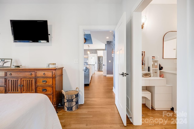 bedroom with stainless steel fridge with ice dispenser, ensuite bathroom, and light hardwood / wood-style floors