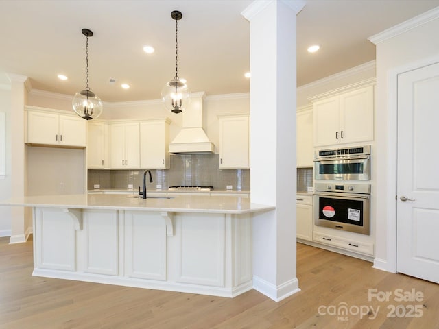 kitchen with pendant lighting, custom range hood, sink, and white cabinets