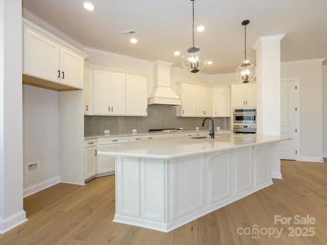 kitchen with light hardwood / wood-style flooring, sink, custom exhaust hood, and a center island with sink