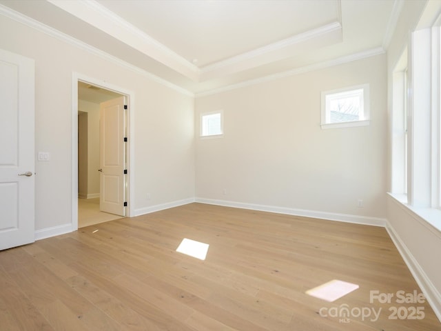 empty room featuring ornamental molding, a tray ceiling, and light hardwood / wood-style flooring