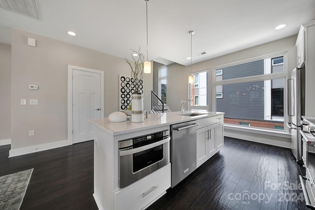 kitchen featuring dark wood-type flooring, stainless steel appliances, a center island with sink, sink, and white cabinets