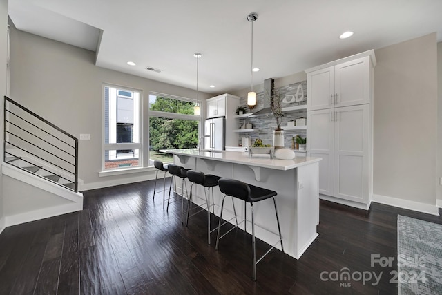 kitchen with an island with sink, high end fridge, dark hardwood / wood-style flooring, hanging light fixtures, and white cabinets