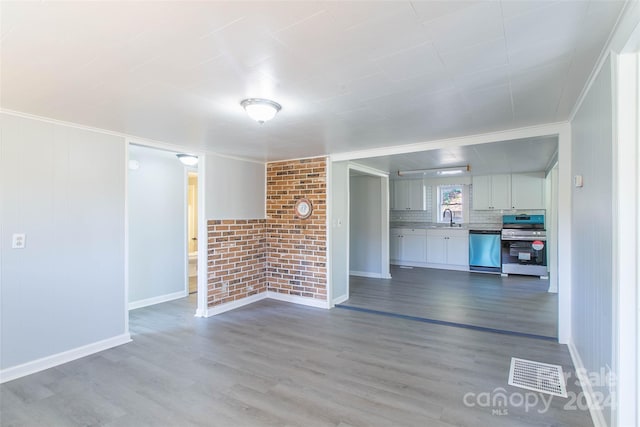 unfurnished living room featuring ornamental molding, sink, hardwood / wood-style flooring, and brick wall