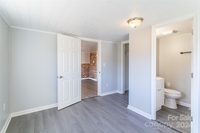 unfurnished bedroom with ensuite bathroom, a closet, brick wall, ornamental molding, and light hardwood / wood-style flooring