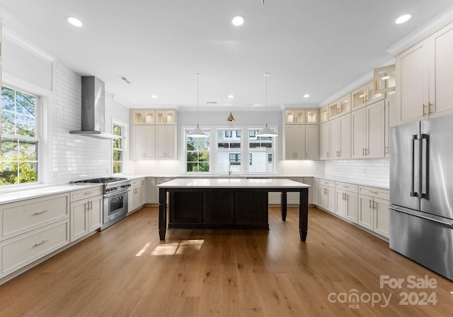 kitchen with a kitchen island, wall chimney exhaust hood, high quality appliances, hanging light fixtures, and light wood-type flooring