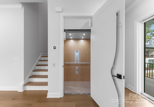 stairs featuring elevator, crown molding, and wood-type flooring