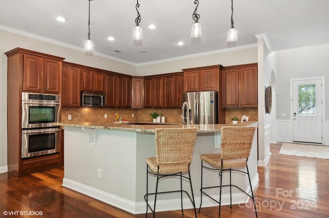 kitchen featuring a large island with sink, hanging light fixtures, a kitchen breakfast bar, stainless steel appliances, and dark wood-type flooring