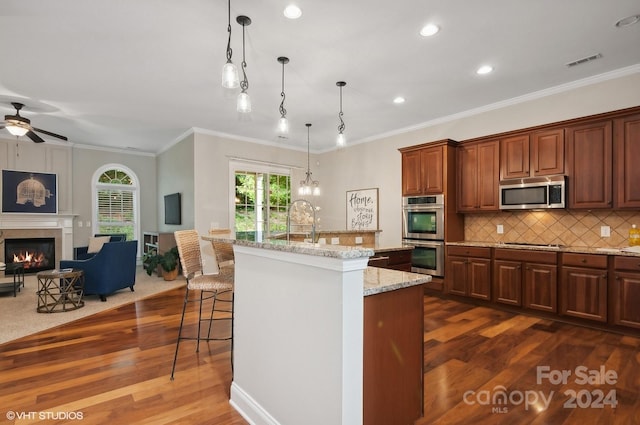 kitchen featuring dark hardwood / wood-style floors, a center island with sink, ornamental molding, pendant lighting, and appliances with stainless steel finishes