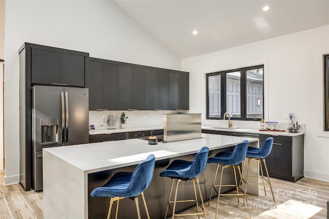 kitchen featuring stainless steel fridge, a kitchen island, a kitchen breakfast bar, light wood-type flooring, and light stone counters