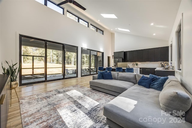 living room with light hardwood / wood-style flooring, a healthy amount of sunlight, high vaulted ceiling, and a skylight