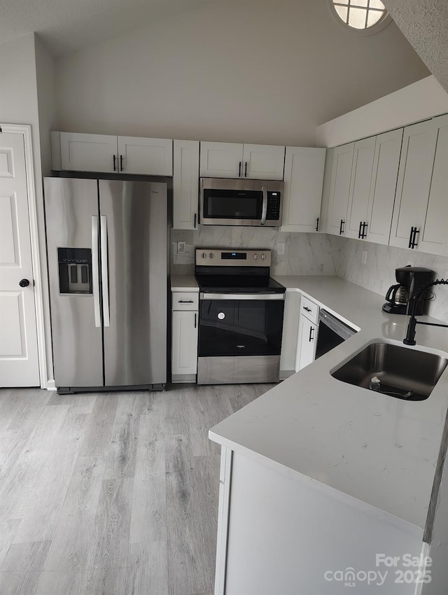 kitchen featuring appliances with stainless steel finishes, light hardwood / wood-style flooring, tasteful backsplash, lofted ceiling, and sink