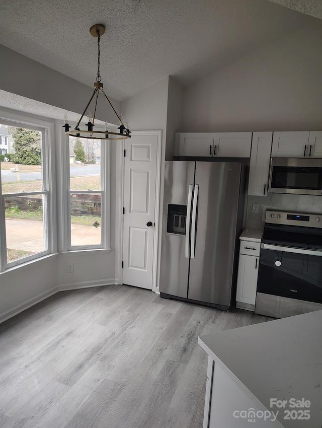 kitchen with vaulted ceiling, light wood-type flooring, pendant lighting, stainless steel appliances, and white cabinets