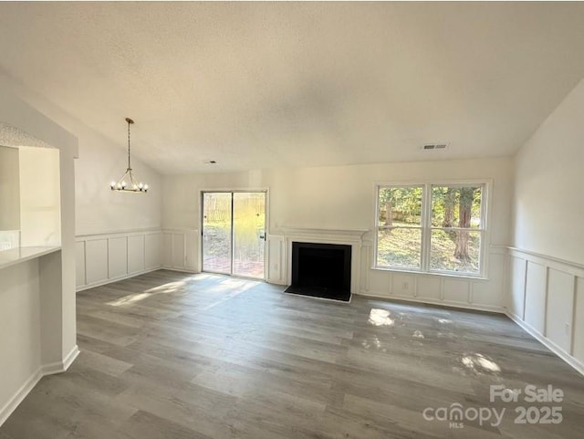 unfurnished living room featuring hardwood / wood-style flooring, a wealth of natural light, a notable chandelier, and lofted ceiling