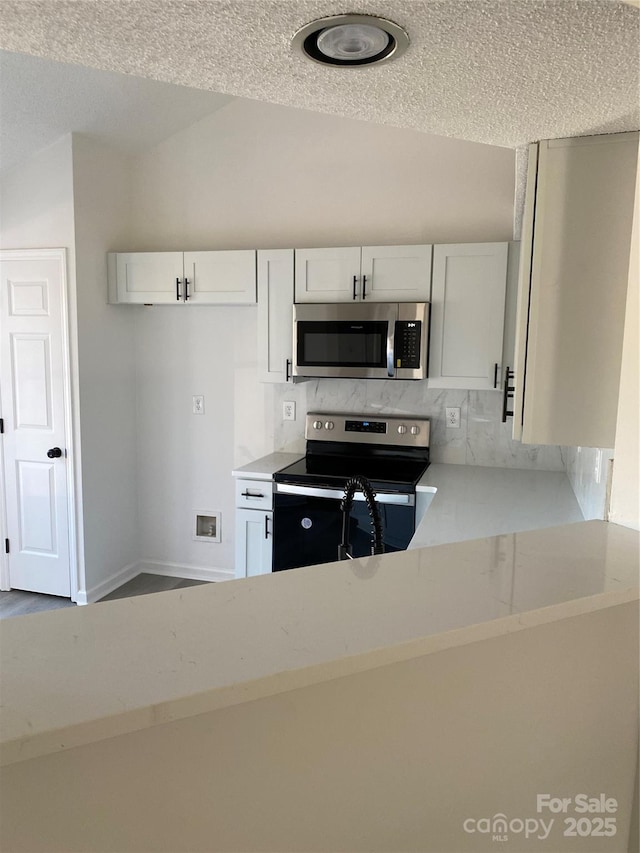 kitchen with white cabinetry, light stone countertops, a textured ceiling, appliances with stainless steel finishes, and decorative backsplash