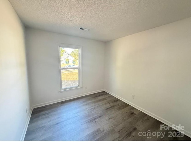 spare room featuring a textured ceiling and dark hardwood / wood-style flooring