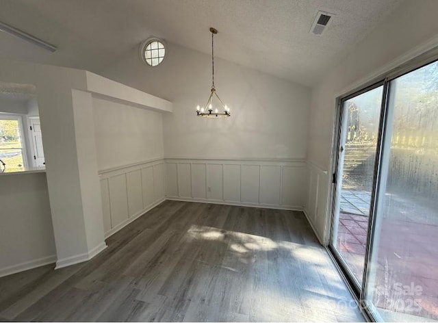 unfurnished dining area with a textured ceiling, vaulted ceiling, an inviting chandelier, and dark hardwood / wood-style flooring