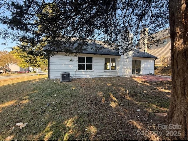 rear view of property featuring central air condition unit and a yard