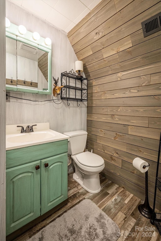 bathroom featuring hardwood / wood-style flooring, vaulted ceiling, toilet, vanity, and wooden walls