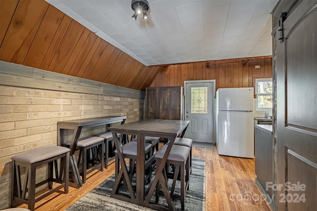 dining area with lofted ceiling, wooden walls, light hardwood / wood-style flooring, and a barn door