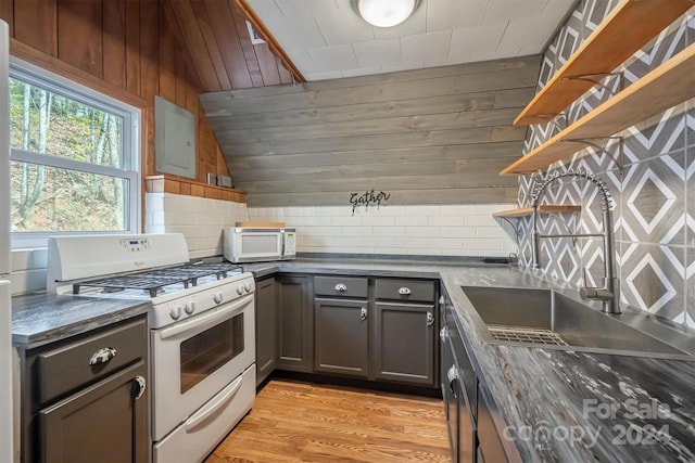 kitchen featuring sink, white gas range oven, light hardwood / wood-style floors, wooden walls, and decorative backsplash