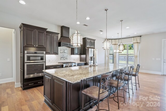 kitchen featuring a large island, a kitchen bar, pendant lighting, light wood-type flooring, and premium range hood