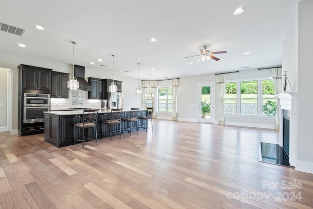 kitchen featuring a large island with sink, custom range hood, a kitchen bar, and a healthy amount of sunlight