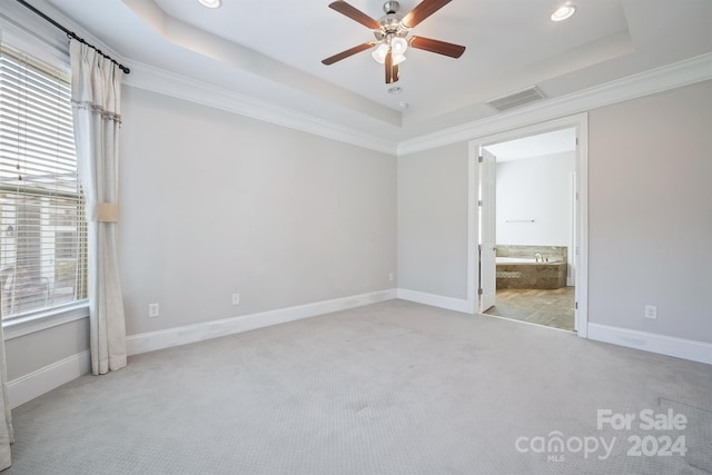 unfurnished bedroom featuring a raised ceiling, ceiling fan, crown molding, ensuite bath, and light colored carpet