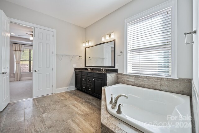 bathroom with vanity, tiled tub, plenty of natural light, and ceiling fan