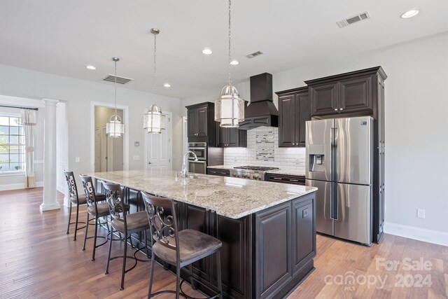 kitchen featuring pendant lighting, an island with sink, ornate columns, and stainless steel appliances