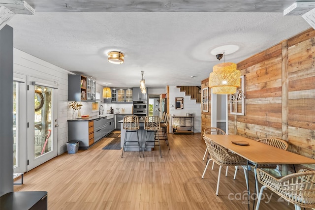 kitchen with wood walls, appliances with stainless steel finishes, pendant lighting, gray cabinets, and light hardwood / wood-style flooring