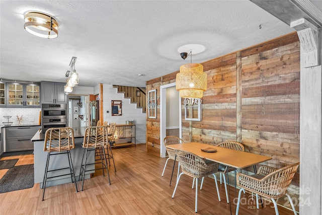 kitchen featuring light wood-type flooring, wood walls, gray cabinetry, decorative light fixtures, and stainless steel appliances